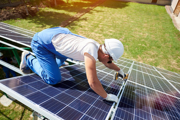 Professional worker installing solar panels on the green metal construction, using different...