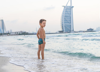 Portrait smiling little baby boy playing in the sea, ocean. Positive human emotions, feelings, joy. Funny cute child making vacations and enjoying summer. Sunset Dubai beach.