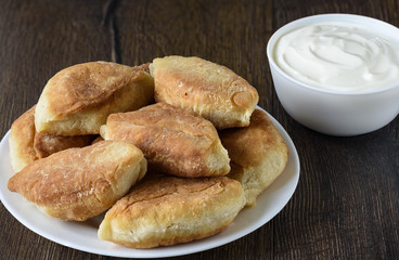Baked pies on a plate. Sour cream in a bowl.