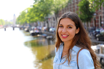 Fototapeta premium Smiling urban girl on bridge looking at camera. Young beautiful woman wearing casual jeans shirt in Amsterdam, Netherlands.