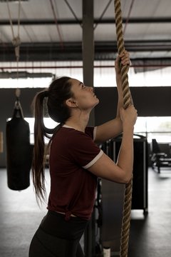 Woman doing rope climbing exercise in fitness gym
