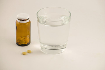 Glass of water and pills from bottle on the white background. A glass of water and vitamins. Healthy lifestyle, nutritional supplements.