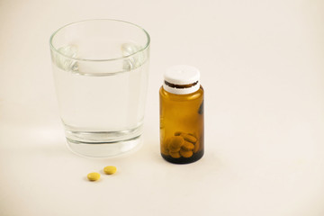 Glass of water and pills from bottle on the white background. A glass of water and vitamins. Healthy lifestyle, nutritional supplements.