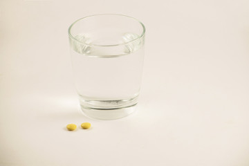 Glass of water and pills on white background. A glass of water and vitamins. Healthy lifestyle, nutritional supplements.
