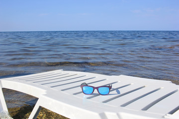sunglasses lie on a deckchair, on a background a blue sea.