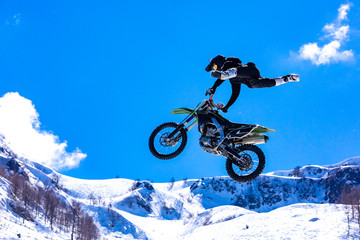 Fototapeta na wymiar racer on a motorcycle in flight, jumps and takes off on a springboard against the snowy mountains