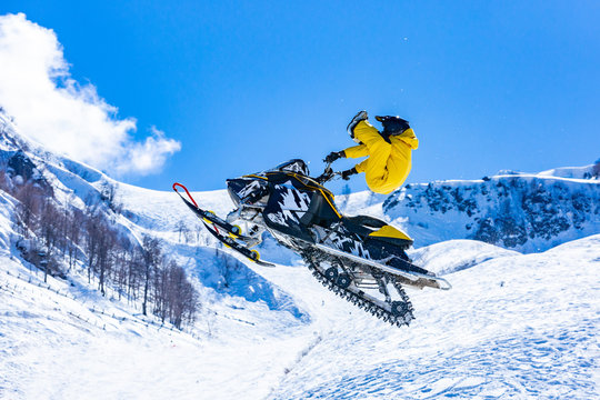 racer on a snow-cat in flight, jumps and takes off on a springboard against the snowy mountains