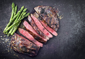 Barbecue dry aged wagyu flank steak sliced with green asparagus as top view on an old rusty board with copy space right