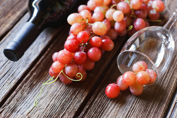 Red grapes, glass, bottle of red wine, cork and corkscrew on vintage wooden background. Close-up, selective focus, shallow depth of field