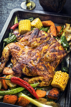 Spatchcocked barbecue chicken al mattone chili with corn and vegetable as top view on an old metal sheet