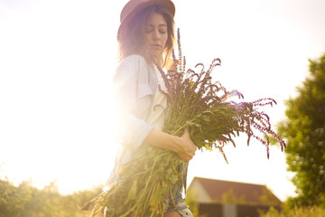 A beautiful girl with a bouquet of lavender. She is dressed in a blue shirt, a white T-shirt. A good summer sunny evening. The girl is smiling. Sunny sunset light