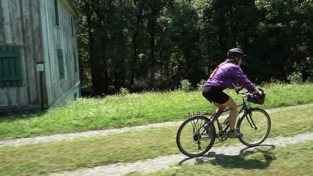 Mature woman bikes past an old building on the C&O Canal National Historic Park near Harpers Ferry, West Virginia.