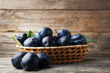Ripe and sweet plums in basket on grey wooden table