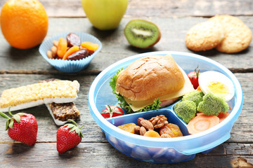 School lunch box with sandwich and vegetables on wooden table