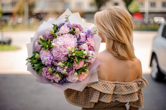 Rear view young beautiful girl holding a bouquet of tender flowers