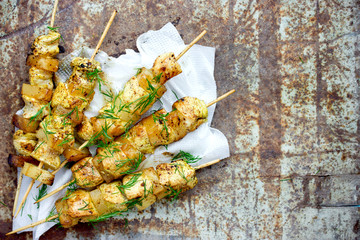 Chicken skewers with pineapple slices with dill and lemon on white paper napkin on an old metal background top view