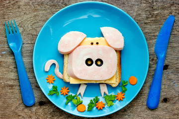 Fun food art idea for kids breakfast - funny pig sandwich with cheese, ham and olives on blue plate top view © san_ta