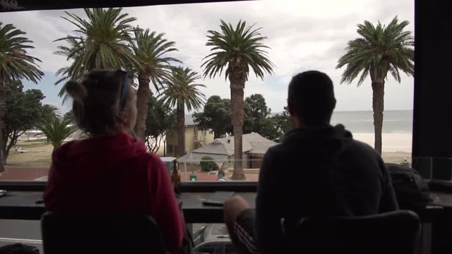 Man and Woman enjoying the view of Palms and Beach from a Terrace in Camps Bay, Cape Town, South Africa in Slow Motion