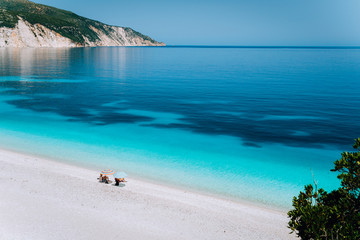 Fteri beach, Kefalonia, Greece. Lonely unrecognizable tourist couple hiding from sun umbrella chill relax near clear blue emerald turquoise sea water lagoon