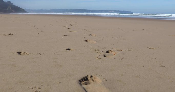 4k video following footprints both feet on sand of Vega Beach seaside next to Ribadesella, Asturias, Spain, Europe
