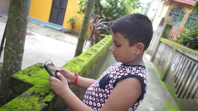 A little asian boy is using his smartphone, or playing games on his smartphone instead of playing, using mobile phones always is not good for health