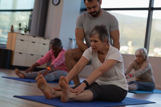Trainer assisting senior women in performing yoga