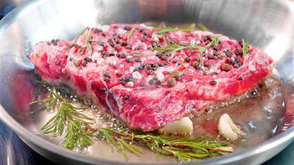 Meat steak with seasonings and herbs hissing on frying pan, close-up