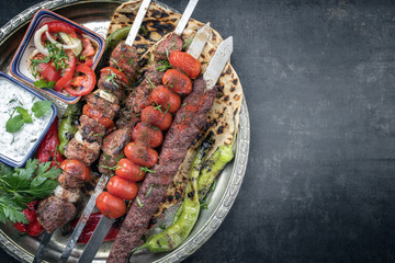 Traditional oriental Adana kebap and shashlik skewer with tomato and flatbread as top view on a plate with copy space right