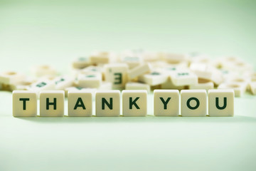 The word THANK YOU on pastel background, spelt with scrabble tiles