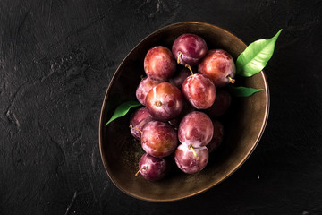 Whole fresh red violet blue plums and slices cut with knife in bowl on kitchen table