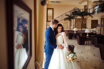 Naklejka premium Beautiful Bride and Groom enjoy each other in the nice hall of the hotel. happy romantic young couple celebrating their marriage.Sexy kissing stylish couple of lovers close up portrait. wedding