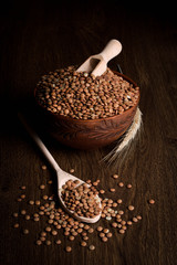 Lentil in a wooden bowl on a wooden background near the ears of wheat. wooden spoon with Lentil