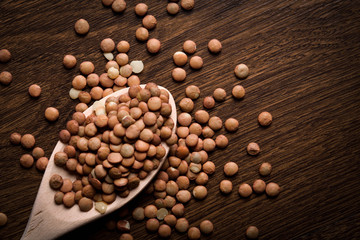 Lentil in a wooden bowl on a wooden background near the ears of wheat. wooden spoon with Lentil