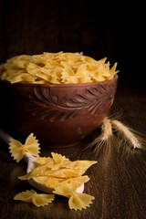 Pasta in the form of a butterfly in a wooden bowl on a wooden background near the ears of wheat. wooden spoon with pasta in the form of a butterfly
