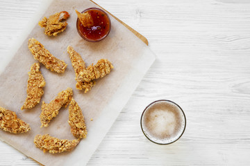 Chicken fingers with sauce and cold beer on white wooden table, overhead view. Space for text.
