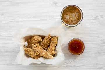 Flat lay of chicken strips with sauce and cold beer on a white wooden table. Overhead, from above.