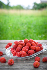 Pink fresh raspberries on an glass vessel on a gray wood background in the garden on the background of green grass Berry Fruit Sadovina Healthy Food hack close up