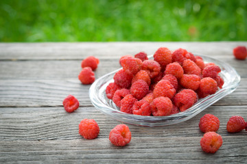 Pink fresh raspberries on an glass vessel on a gray wood background in the garden on the background of green grass Berry Fruit Sadovina Healthy Food hack close up