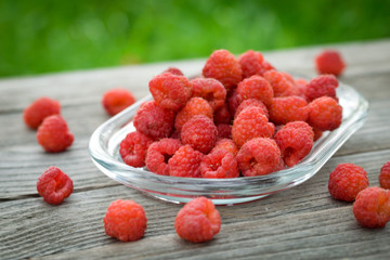 Pink fresh raspberries on an glass vessel on a gray wood background in the garden on the background of green grass Berry Fruit Sadovina Healthy Food hack close up