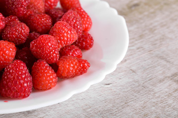 Red fresh raspberries on white rustic wood background. Plate with natural ripe organic berries.flat lay with copy space