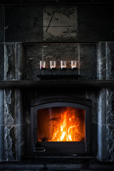 Fireplace made of black stone with fire and candles on the shelf
