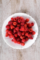  Red fresh raspberries on white rustic wood background. Plate with natural ripe organic berries.flat lay with copy space top view