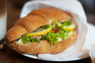 Freshly croissant with tuna, lemon and salad on wooden background. Breakfast concept.