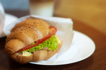 Fresh croissant with ham, tomato and salad leaf. concept of a morning breakfast. Copy space