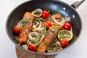 Salmon fried in a pan with onions, lemon and cherry tomatoes