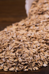 Oat flakes scattered on the table from an overturned white bowl, close-up, vertical frame.