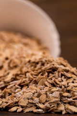 Oatmeal close-up on the table on the background of a tilted white bowl closeup on wooden background, vertical shot.