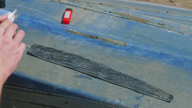 Process of reparing canoe. Man tapes hole on bottom of canoe