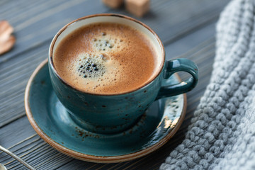 Blue cup whith coffee, knitted sweater, autumn leaves on wooden background. Cozy morning.