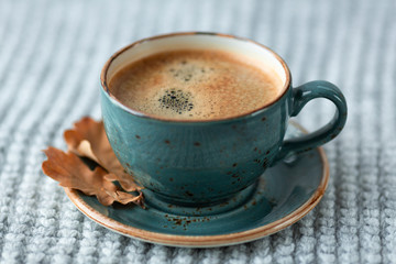 Blue cup whith coffee, knitted sweater, autumn leaves on wooden background. Cozy morning.